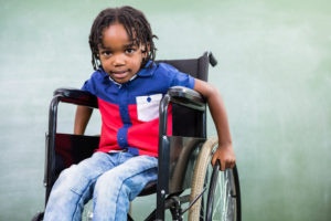 A child sitting in a wheelchair, leaning forward to hold onto the wheels